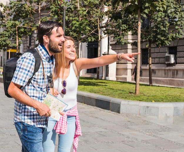 Hombre con mapa mirando a mujer feliz apuntando hacia algo