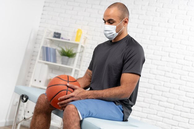 Hombre con máscara médica y baloncesto en fisioterapia