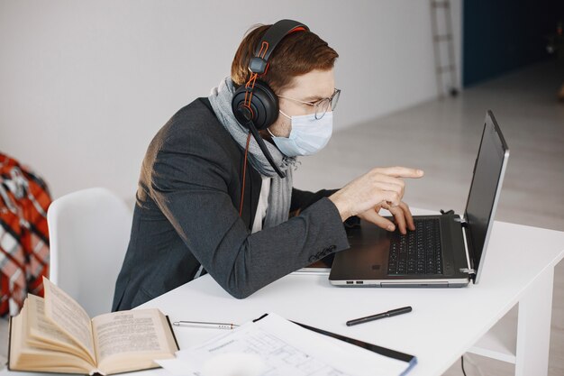 Hombre con una máscara médica. Hombre sentado en la sala de estar en casa. Guy disfruta estudiando en cuarentena.