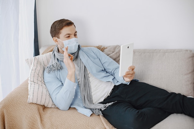 Hombre con una máscara médica. Hombre sentado en la sala de estar en casa. Guy disfruta estudiando en cuarentena.