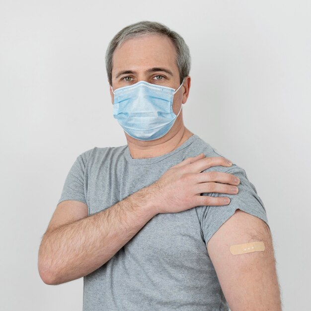 Hombre con máscara médica mostrando vendaje en el brazo después de la vacunación