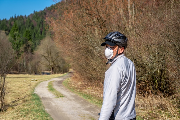 Hombre con máscara protectora en la cara montando bicicleta durante el coronavirus / covid-19