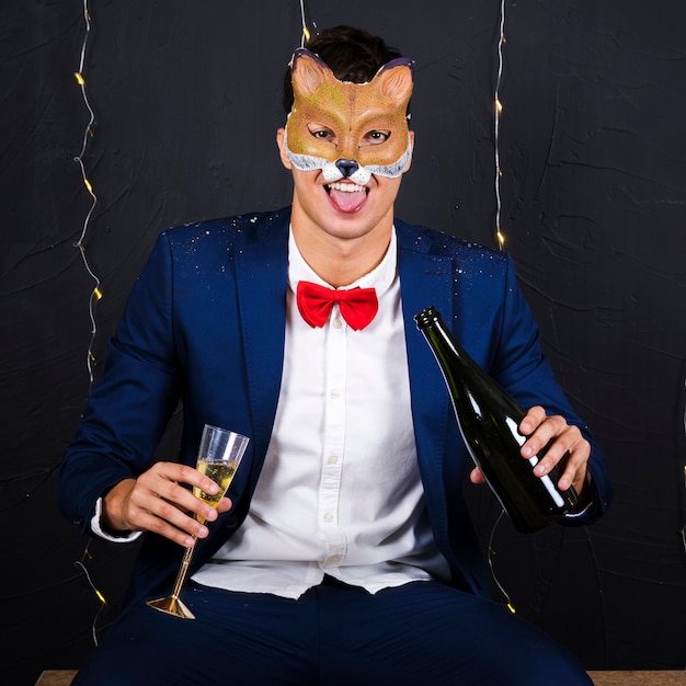 Hombre en máscara de zorro con vaso y botella de champagne