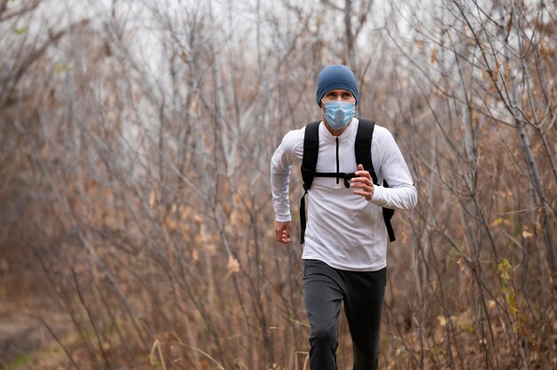 Hombre con mascarilla corriendo en el bosque