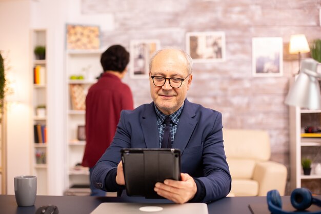 Hombre mayor de 60 años usando una tableta digital moderna en su acogedora casa