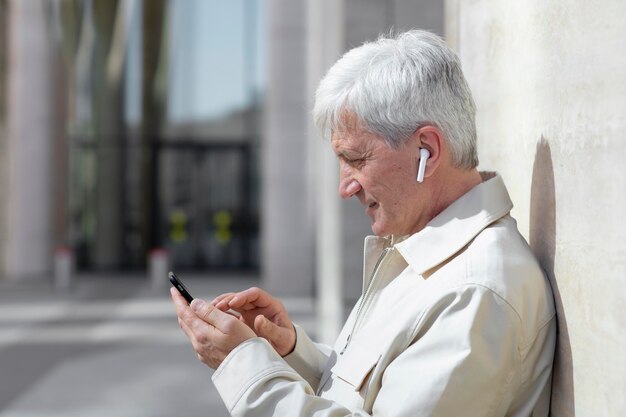 Hombre mayor al aire libre en la ciudad con smartphone con auriculares