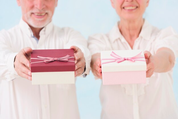 Hombre mayor alegre y mujer que dan la caja de regalo