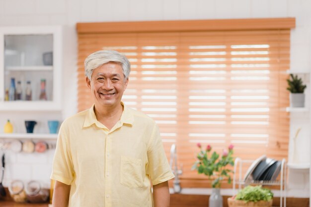 Hombre mayor asiático que siente la sonrisa feliz y que mira a la cámara mientras que relájese en cocina en casa. Estilo de vida de los hombres mayores en el concepto de casa.