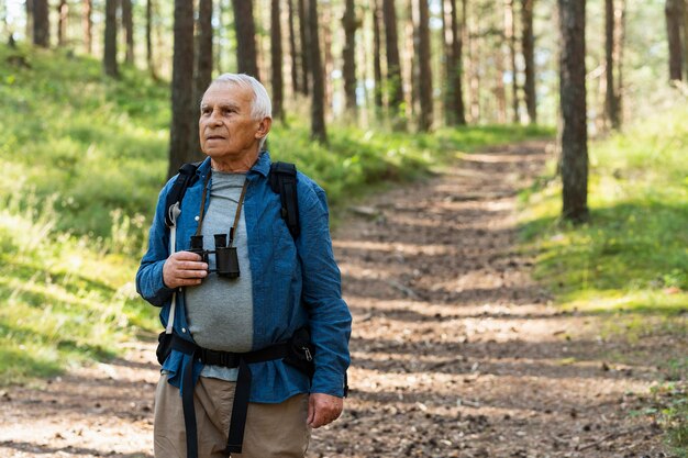 Hombre mayor con binoculares y mochila explorando la naturaleza