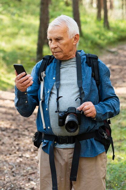 Hombre mayor con cámara y smartphone al aire libre en la naturaleza