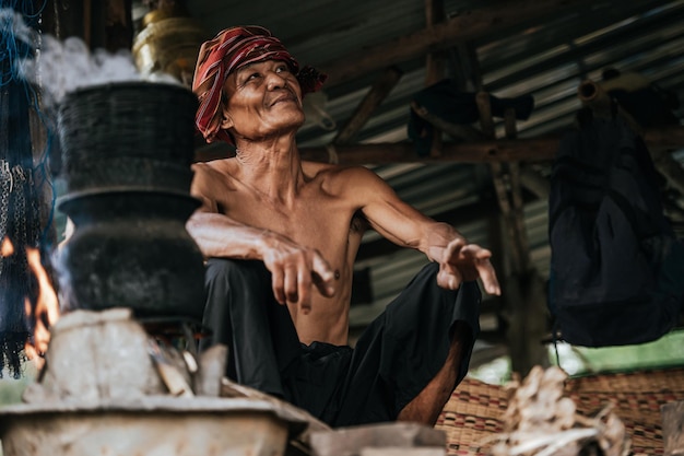 Hombre mayor sin camisa y taparrabos de turbante arroz pegajoso al vapor con una estufa de leña según la vida de la gente rural, espacio de copia, escena rural del campo en Tailandia