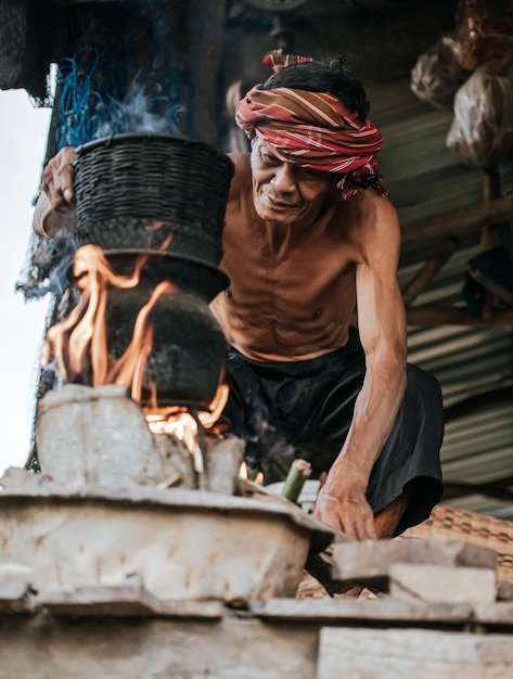 Hombre mayor sin camisa y taparrabos de turbante arroz pegajoso al vapor con una estufa de leña según la vida de la gente rural, espacio de copia, escena rural del campo en Tailandia