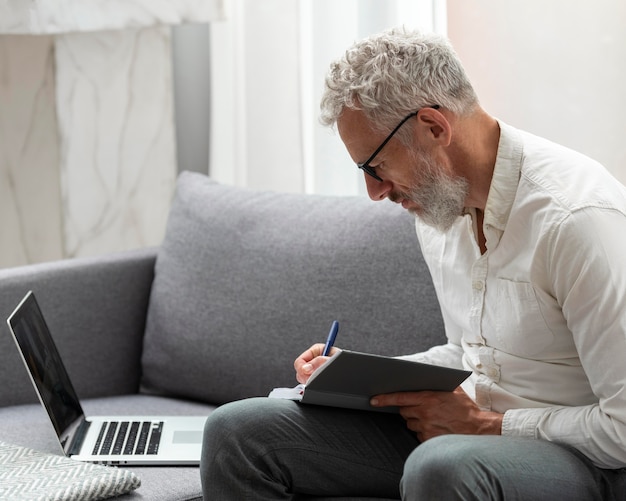 Hombre mayor en casa estudiando en el portátil y tomando notas
