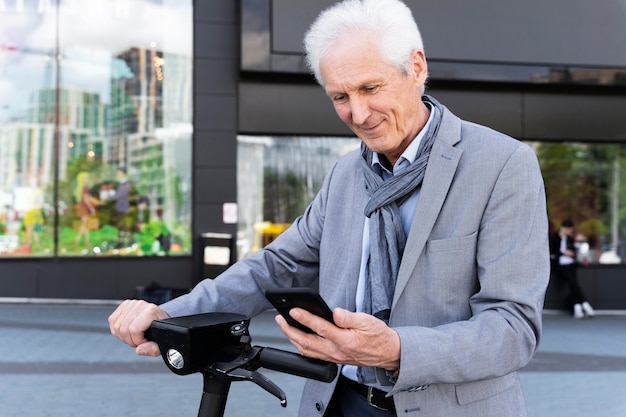 Hombre mayor en la ciudad con scooter eléctrico con smartphone