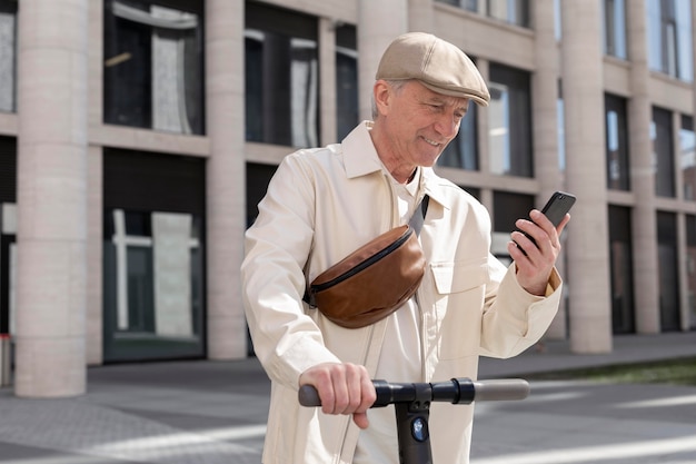 Hombre mayor en la ciudad con un scooter eléctrico con smartphone