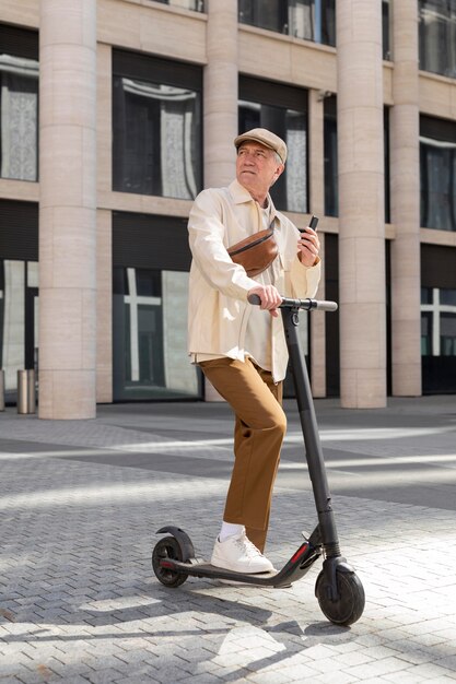 Hombre mayor en la ciudad con un scooter eléctrico con smartphone