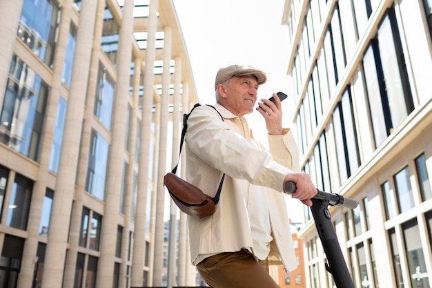 Hombre mayor en la ciudad con un scooter eléctrico con smartphone