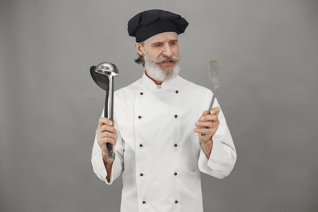 El hombre mayor elige cucharas. Chef con una gorra negra en la cabeza. Enfoque profesional de los negocios.