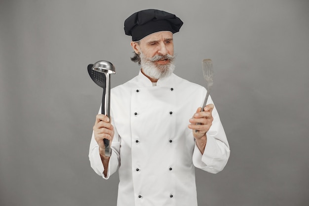 El hombre mayor elige cucharas. Chef con una gorra negra en la cabeza.