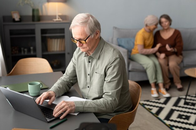 El hombre mayor está usando una computadora portátil sentada en el escritorio en la sala de estar