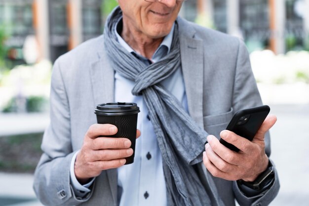 Hombre mayor con estilo en la ciudad con smartphone mientras toma café