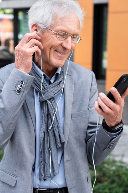 Hombre mayor con estilo en la ciudad con teléfono inteligente y auriculares para videollamada