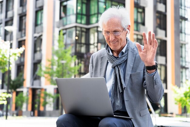 Hombre mayor con estilo en la ciudad usando laptop para videollamada
