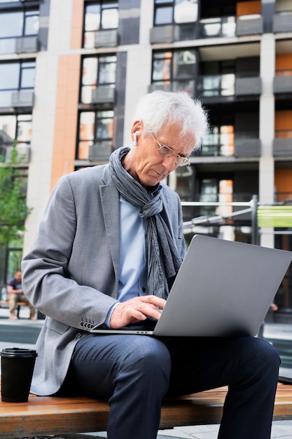 Hombre mayor con estilo en la ciudad usando laptop