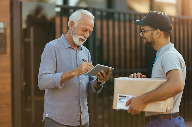 Hombre mayor feliz que usa el panel táctil y firma para una entrega del servicio de mensajería