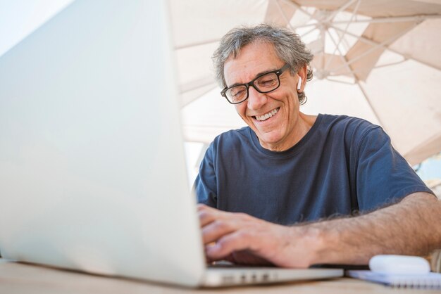 Hombre mayor feliz usando anteojos usando laptop en cafés al aire libre