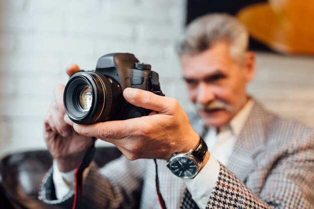 Hombre mayor, fotógrafo profesional sostiene una vieja cámara de fotos mientras pasa tiempo en la cafetería moderna.