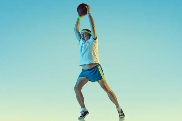 Hombre mayor jugando baloncesto sobre fondo degradado en luz de neón. Modelo masculino caucásico en gran forma se mantiene activo, deportivo.