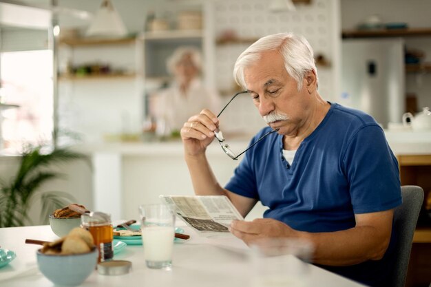 Hombre mayor leyendo el periódico mientras desayuna en casa