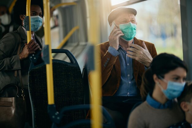 Hombre mayor con mascarilla hablando por teléfono mientras viaja en autobús