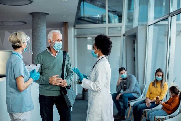 Hombre mayor con mascarilla protectora hablando con médicos en el pasillo del hospital