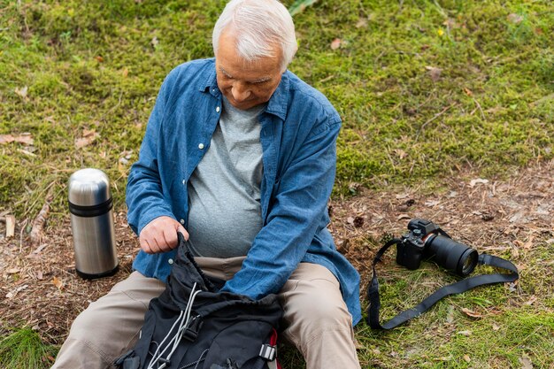 Hombre mayor con mochila y cámara descansando mientras explora la naturaleza