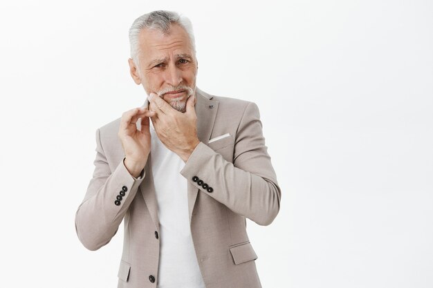 Hombre mayor molesto en chaqueta tocando la mandíbula, quejándose de dolor de muelas