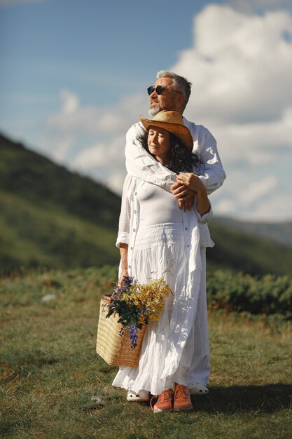 Hombre mayor y mujer en las montañas. Mujer con canasta de flores. Hombre con camisa blanca.