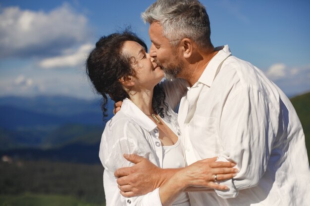 Hombre mayor y mujer en las montañas. Pareja adulta enamorada al atardecer. Hombre con camisa blanca.