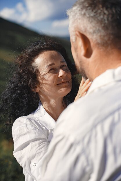 Hombre mayor y mujer en las montañas. Pareja adulta enamorada al atardecer. Hombre con camisa blanca.