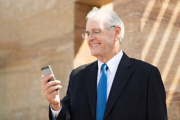 Foto gratuita hombre mayor de negocios mirando su teléfono y sonriendo