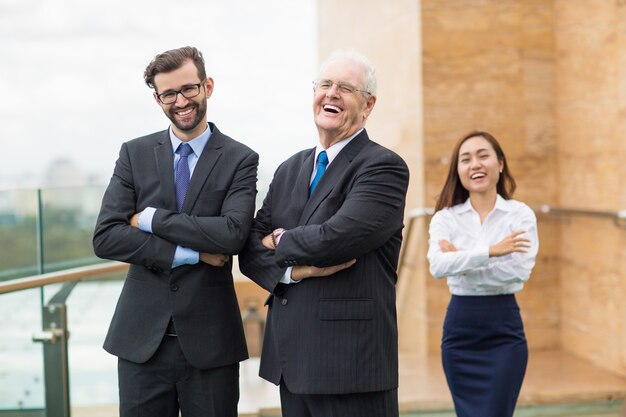 Hombre mayor de negocios riendo junto a un hombre y una mujer de negocios más joven
