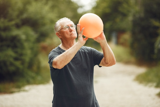 Hombre mayor en el parque de verano. Grangfather usando una pelota.