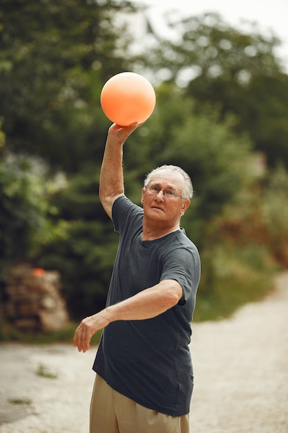 Hombre mayor en el parque de verano. Grangfather usando una pelota.