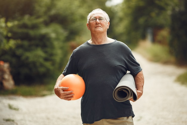 Hombre mayor en el parque de verano. Grangfather usando una pelota.