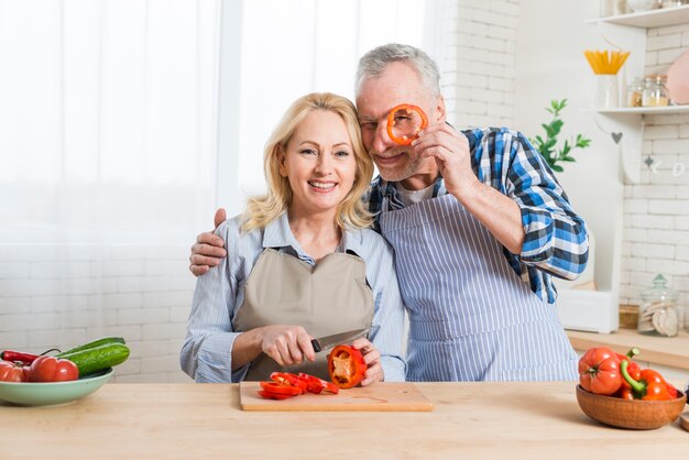 Hombre mayor que lleva a cabo la rebanada del paprika rojo delante de sus ojos en la cocina