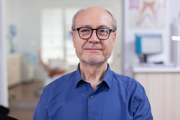 Hombre mayor que mira la cámara en el consultorio dental wainting consulta hombre mayor sonriendo en la cámara web s ...