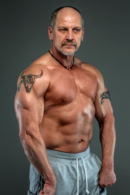 Hombre mayor que muestra los músculos. Sesión de estudio. aislado en gris oscuro