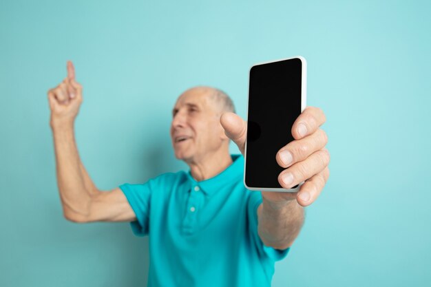 Hombre mayor que muestra la pantalla del teléfono en blanco