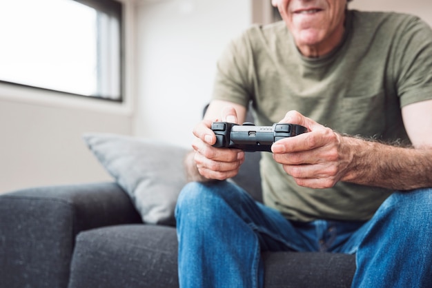 Hombre mayor que se sienta en el sofá que juega al videojuego en casa